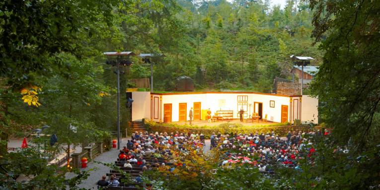 Open-Air-Bühne mit Zuschauerreihen von Wald umgeben.